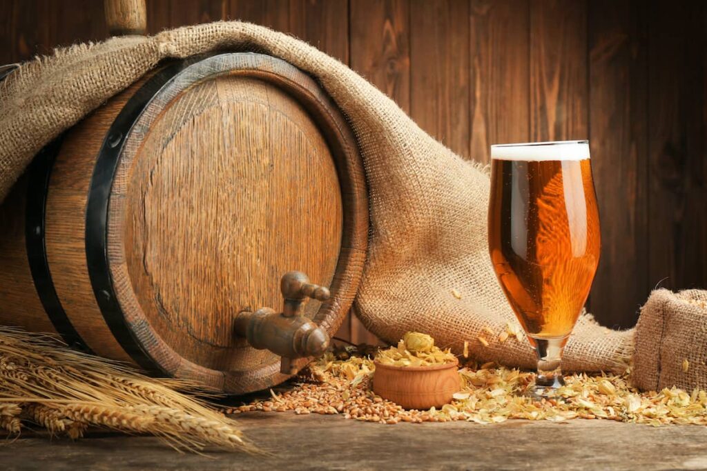 Cerveza artesanal servida en copa con lúpulo y barril de madera